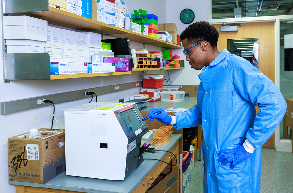 A scientist at a lab bench enters settings on a machine involved in Immune Health research.